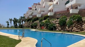A swimming pool with a stone wall and palm trees. - Apartment Mar de Nerja Sunset (Nerja)