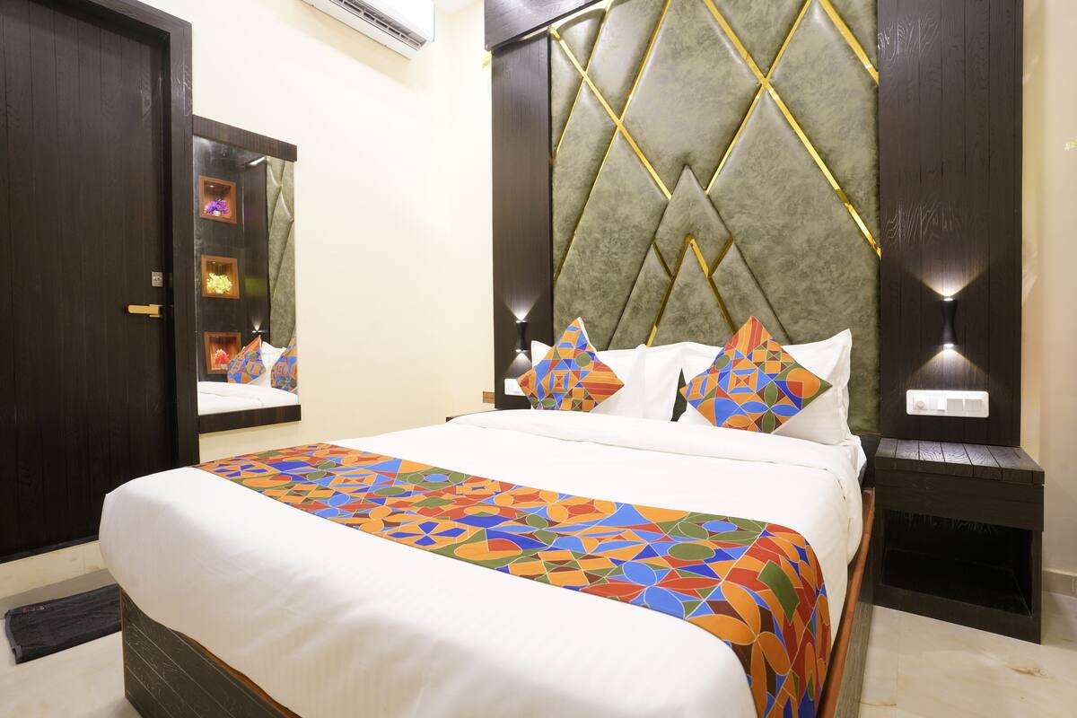 A neatly made bed with a colorful geometric-patterned bedspread, a large mirror, and a wall with a geometric-patterned headboard.
