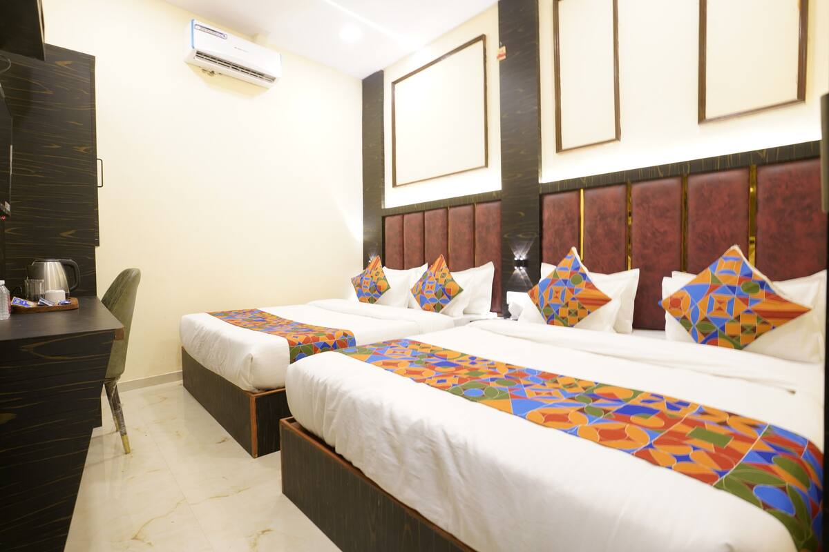 A hotel room with two beds, a desk, and an air conditioning unit.