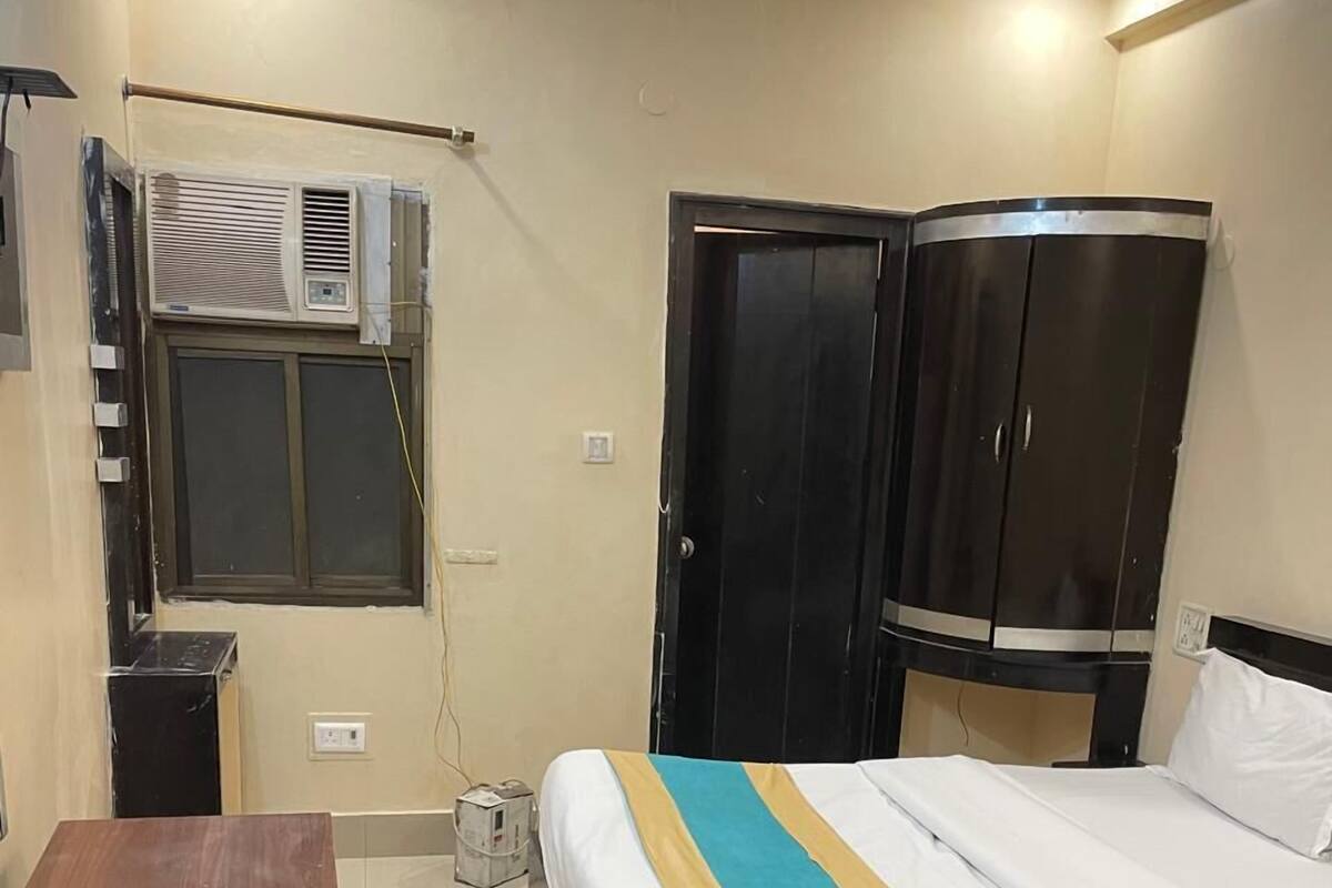 A bedroom with a bed, a desk, a wardrobe, and an air conditioning unit.
