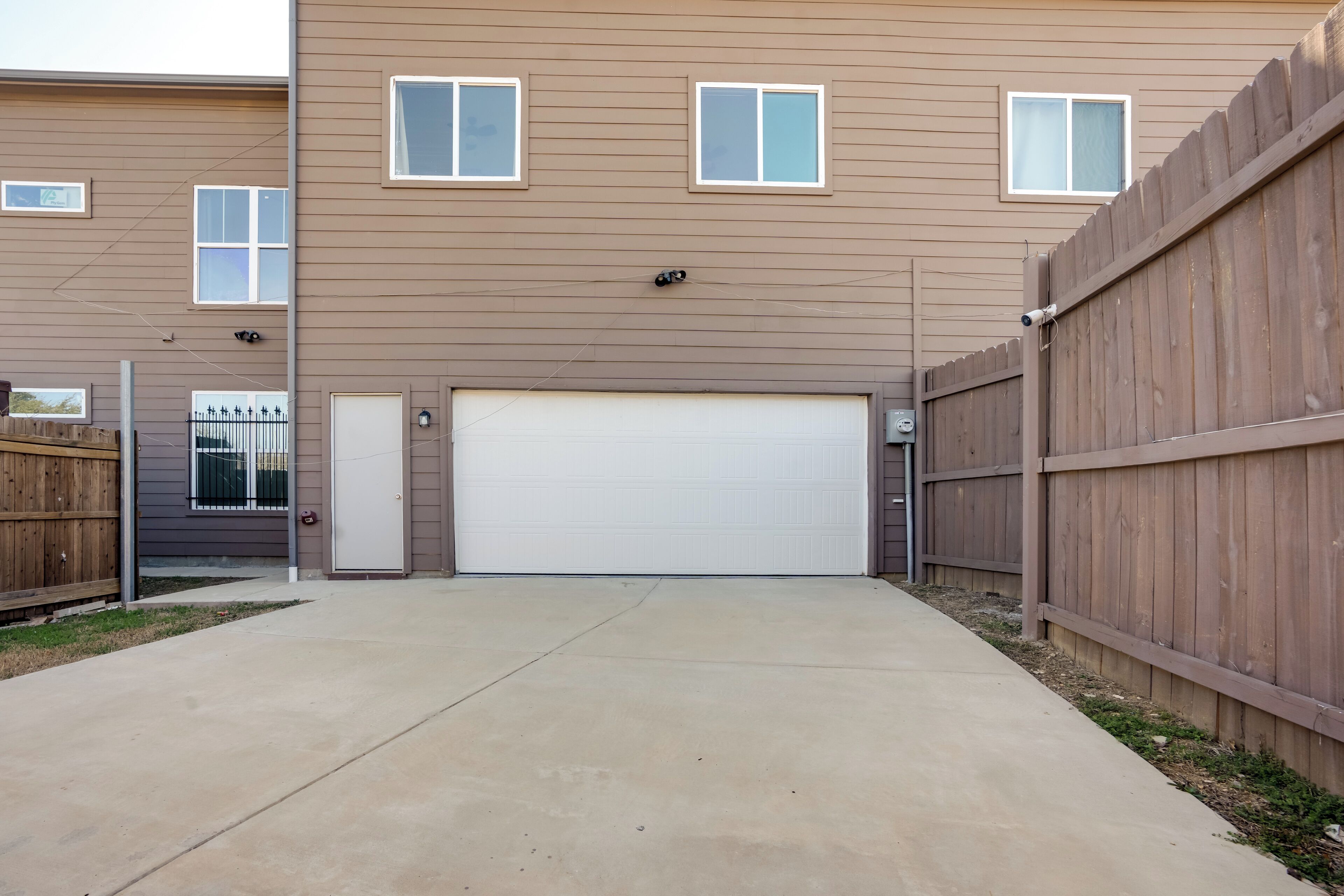 A residential building with a garage, a wooden fence, and a concrete driveway.