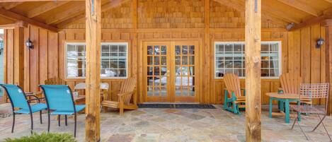 A wooden cabin with a stone patio, wooden chairs, and a wooden table.