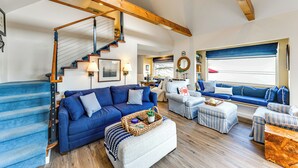 Amplia sala de estar con un sofá azul, sillones a rayas, una escalera de madera y un ventanal con vistas.