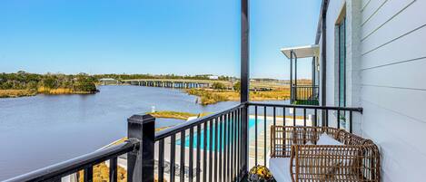 A balcony with a view of a river and a bridge, wicker furniture, and a small pool.