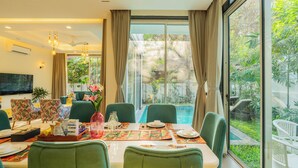 A dining area with a table set for four, chairs, and a view of a swimming pool and greenery outside. - ELIVAAS Laguna Camellia | Luxe 4 BHK Villa Near Popular Beaches with Private Pool (Anjuna)