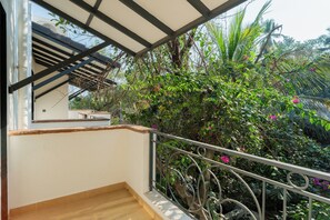 Un balcón con piso de madera y baranda metálica, con vista a un jardín exuberante lleno de plantas y flores.