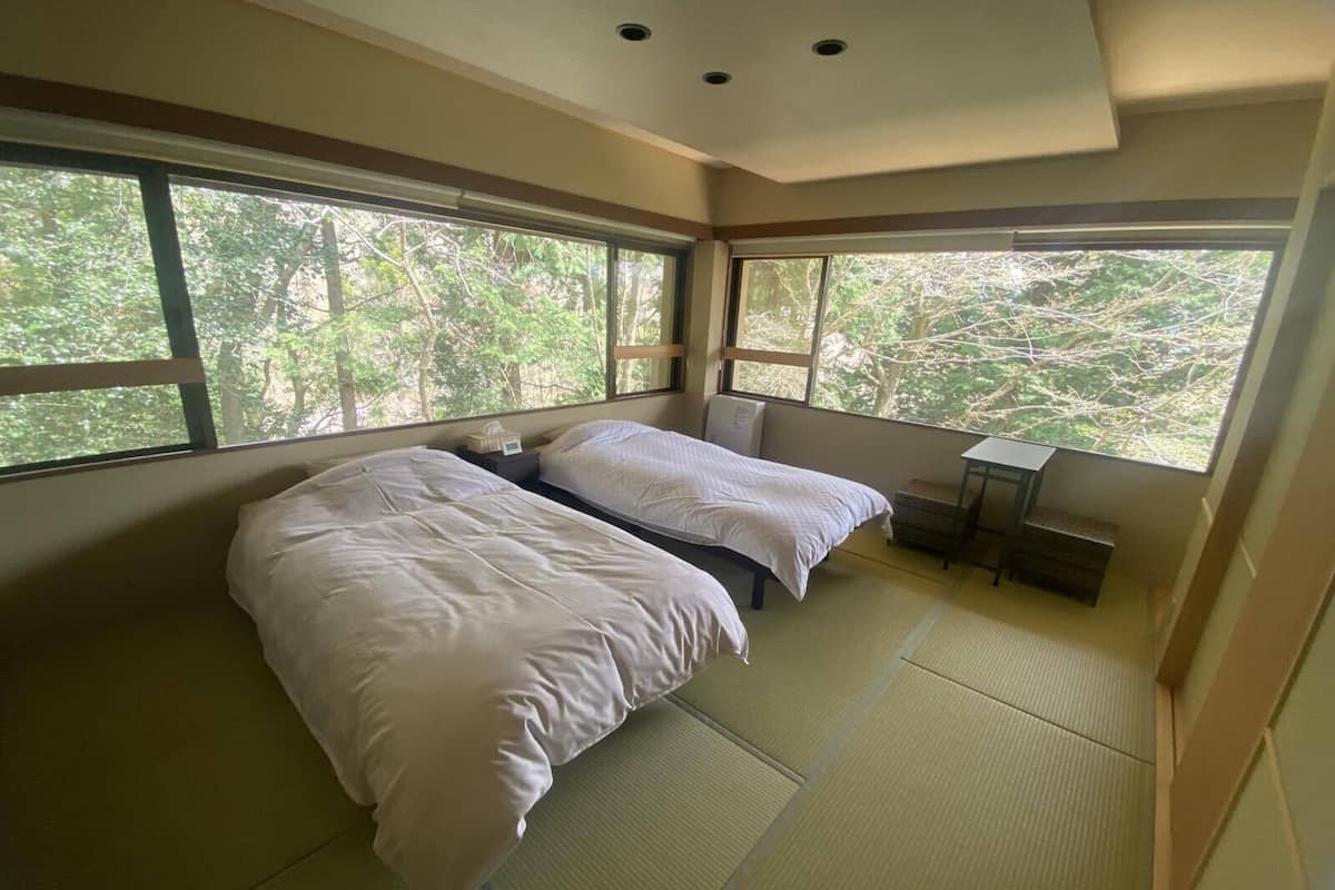 A bedroom with two beds, large windows, tatami flooring, and a small table.