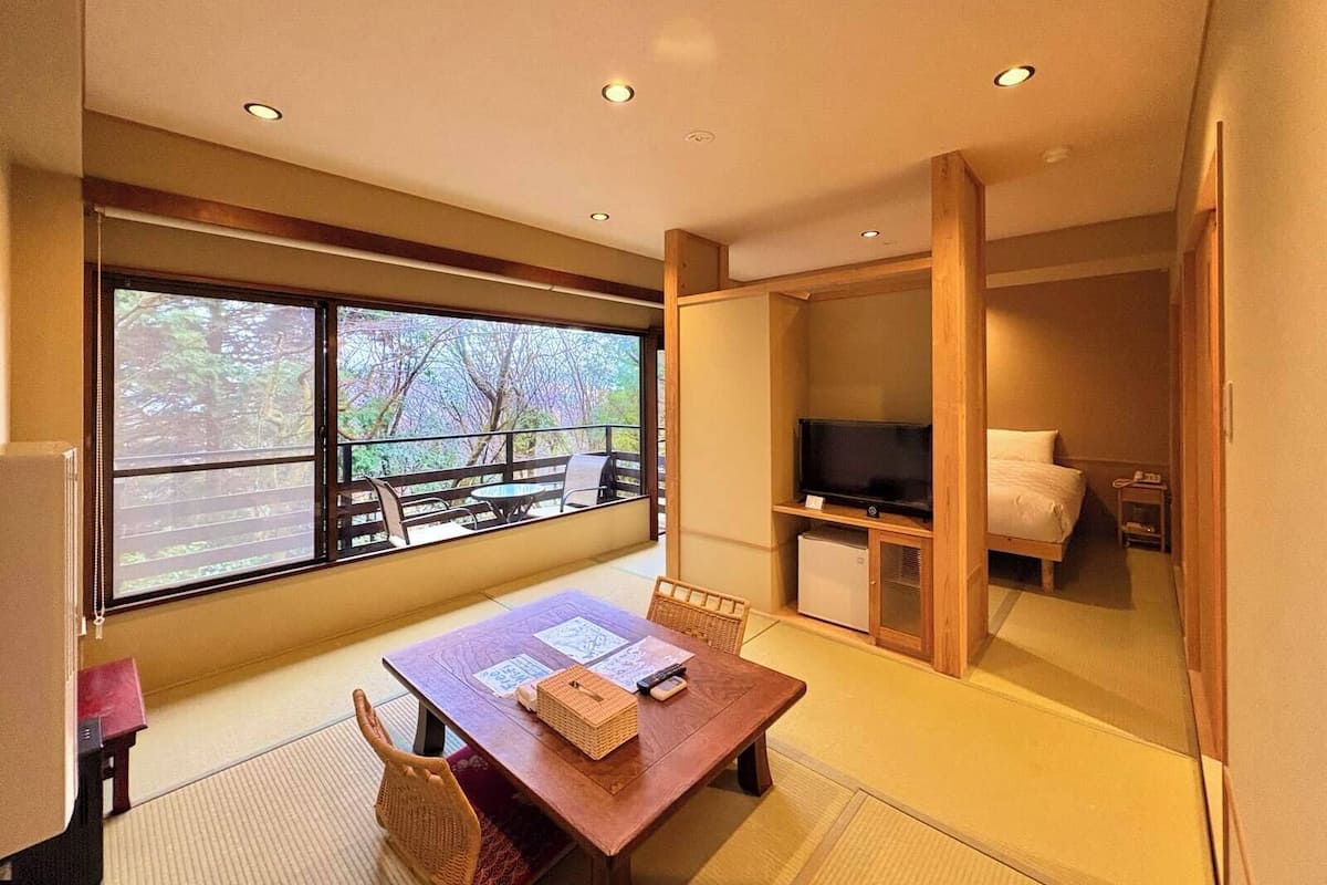 A hotel room with a large window, a wooden dining table, a television, and a bed.