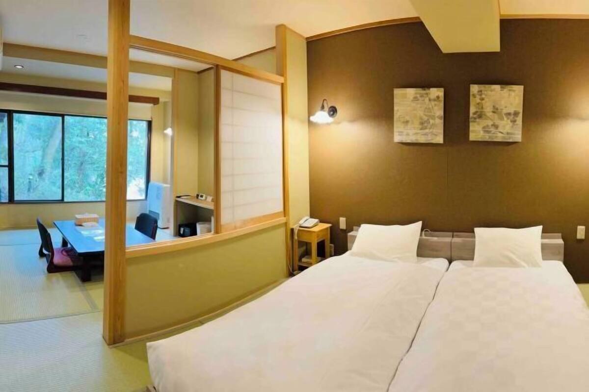 A hotel room with a large bed, a desk, a chair, and a view of trees through the window.
