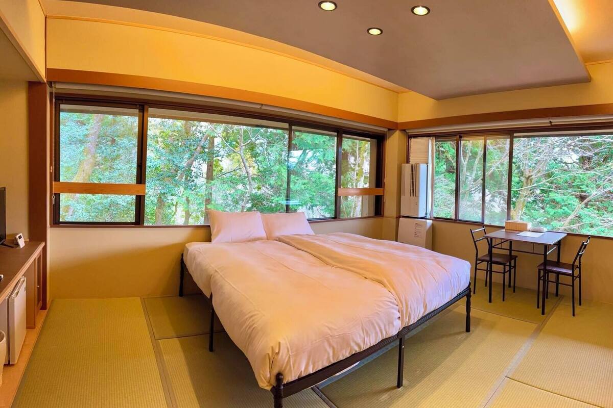 A bedroom with a bed, a desk, and large windows.