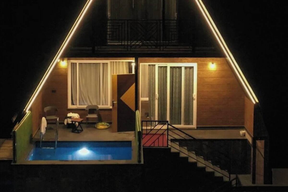 A triangular-shaped house with a pool, a balcony, and a staircase leading to the entrance.