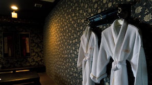 A bathroom with two white bathrobes hanging on a rack, a mirror, and a patterned wall.