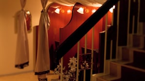 A staircase with a dark handrail and white balusters, leading to a room with a red wall and a white curtain.