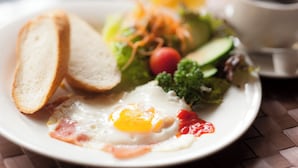 A plate with a fried egg, toast, vegetables, and a cup of coffee.