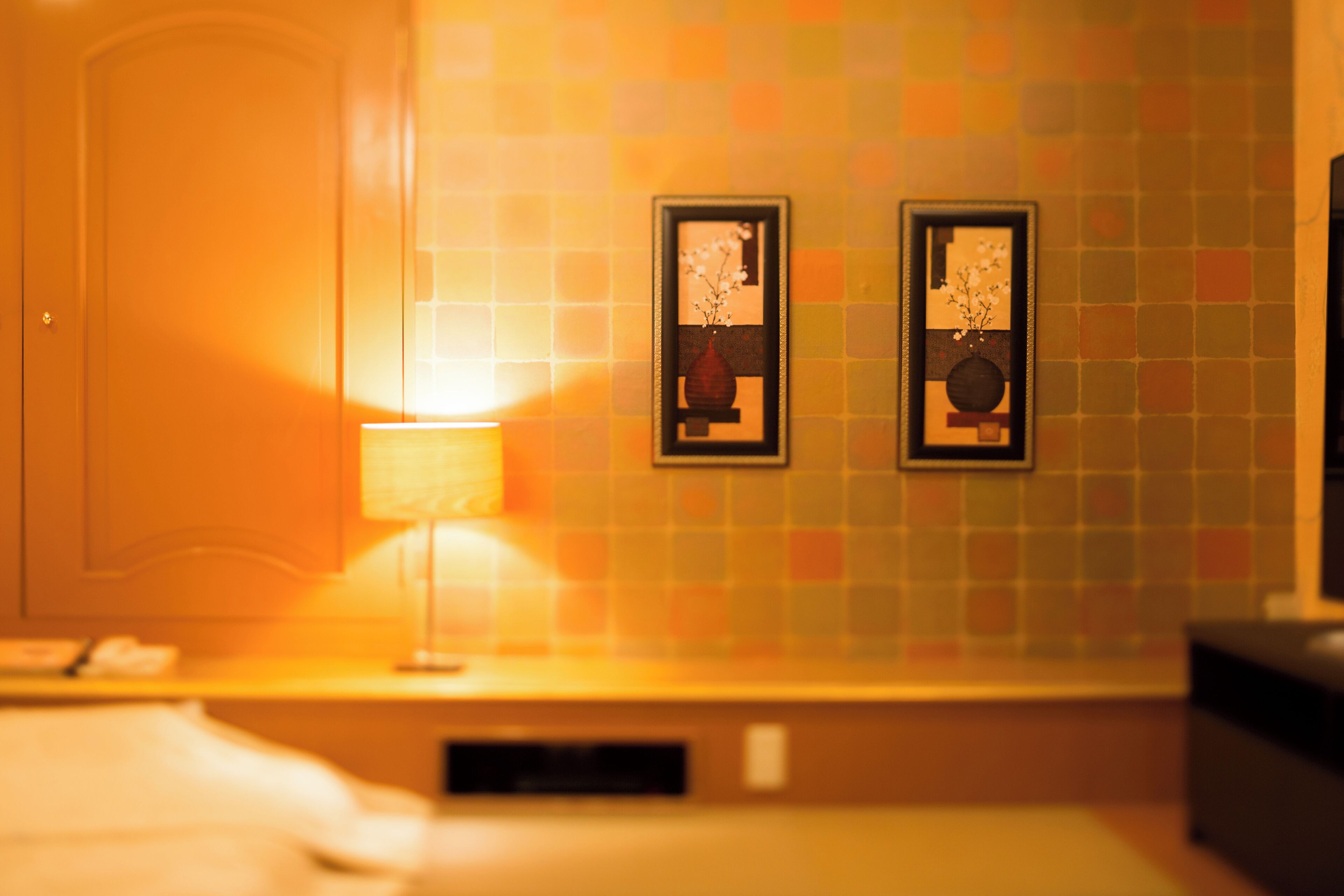 A hotel room with a bed, a nightstand, a lamp, and two framed pictures on the wall.