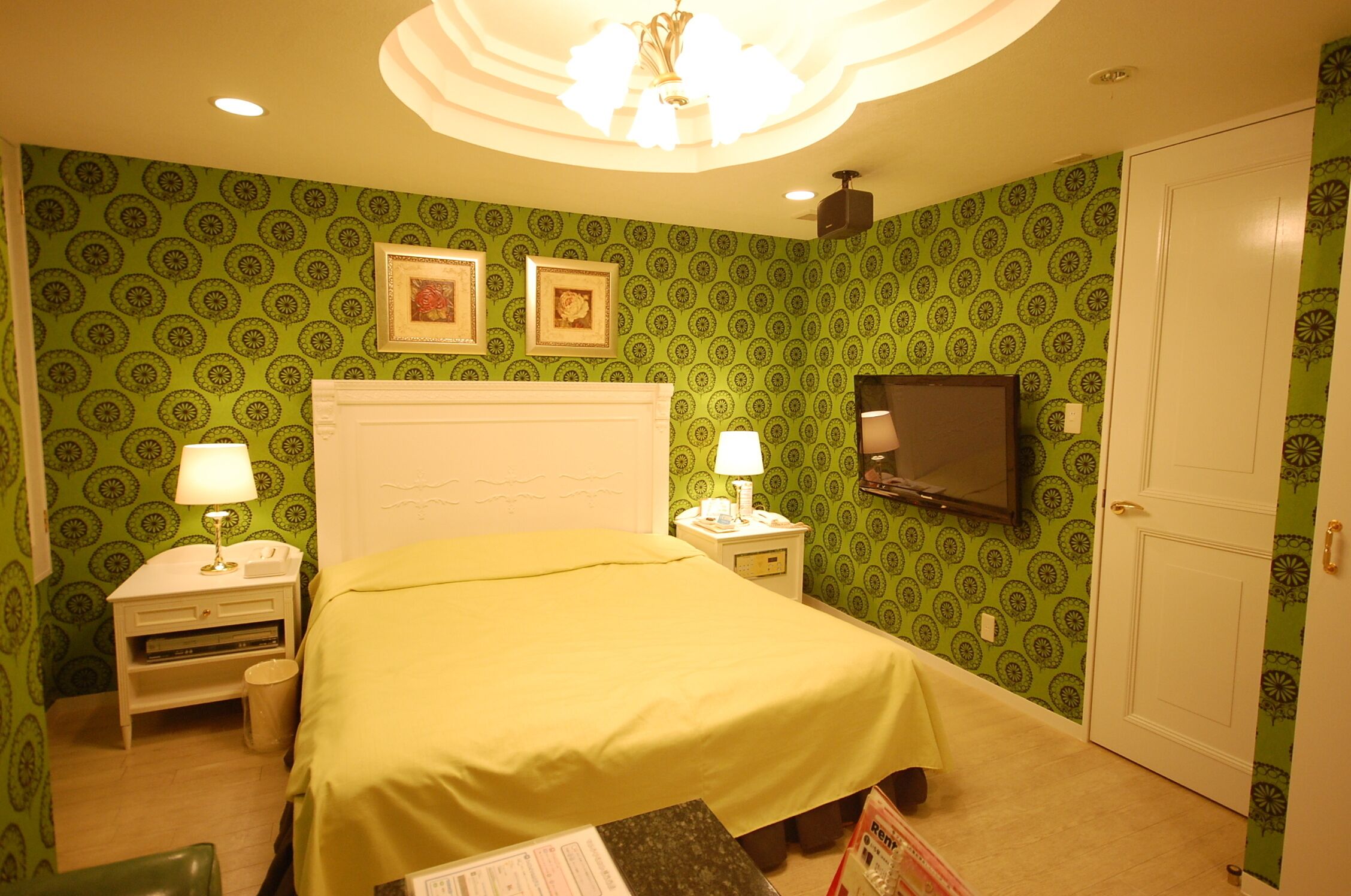 A hotel room with a bed, two bedside tables with lamps, a television mounted on the wall, and a door.