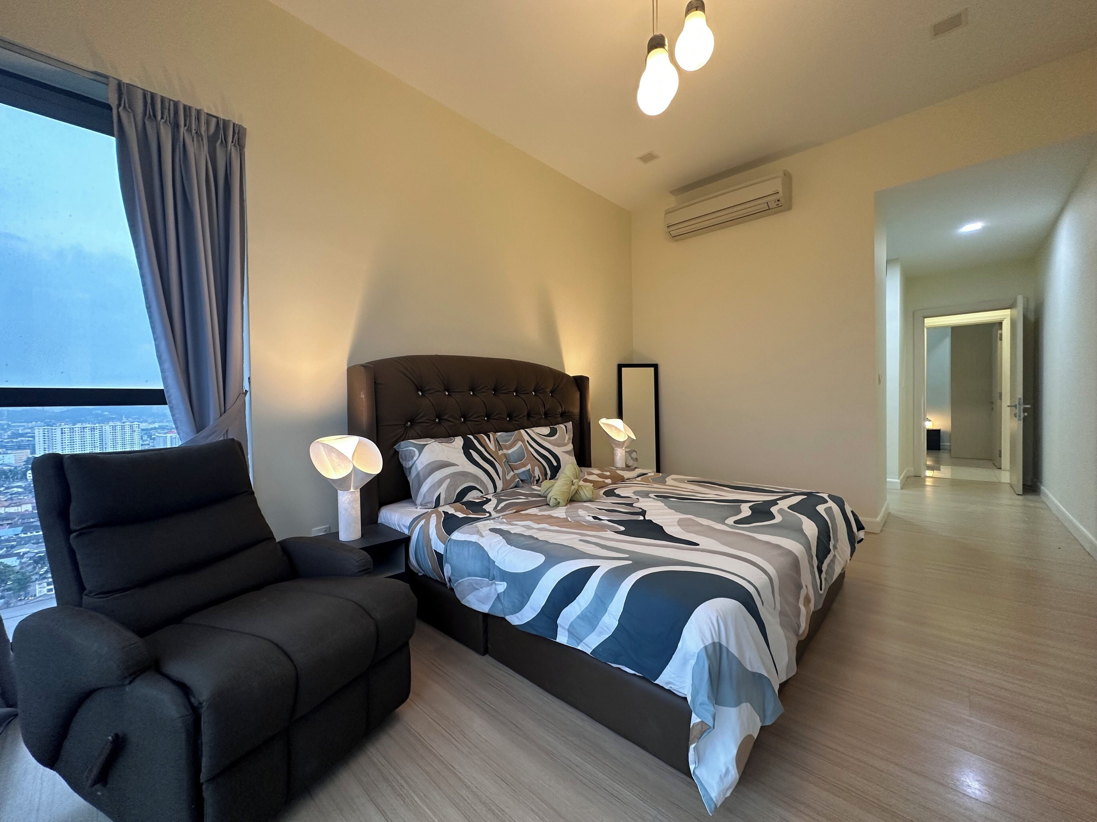 A modern bedroom with a large bed, a sitting area, and a view of the city.
