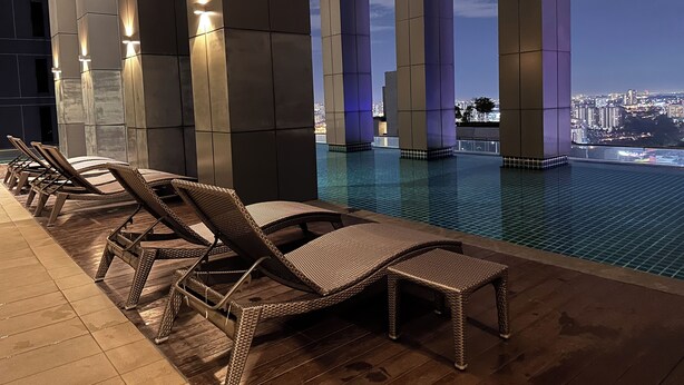 A rooftop pool area with lounge chairs and a view of the city skyline at dusk. - Skyline Luxe 4BR Retreat with En-suites (Petaling Jaya)