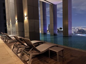 Un área de piscina en la azotea con sillas de descanso y vistas del horizonte urbano al anochecer.