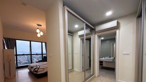 A modern bedroom with a large window, a bed, a sliding glass door leading to a bathroom, and an air conditioning unit on the wall. - Skyline Luxe 4BR Retreat with En-suites (Petaling Jaya)