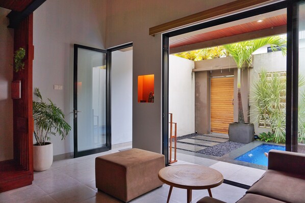 Un intérieur moderne avec une porte vitrée donnant sur une cour intérieure agrémentée d’une piscine et de plantes.