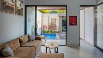 Un salón moderno con sofá, una mesita redonda y vistas a una piscina y jardín.