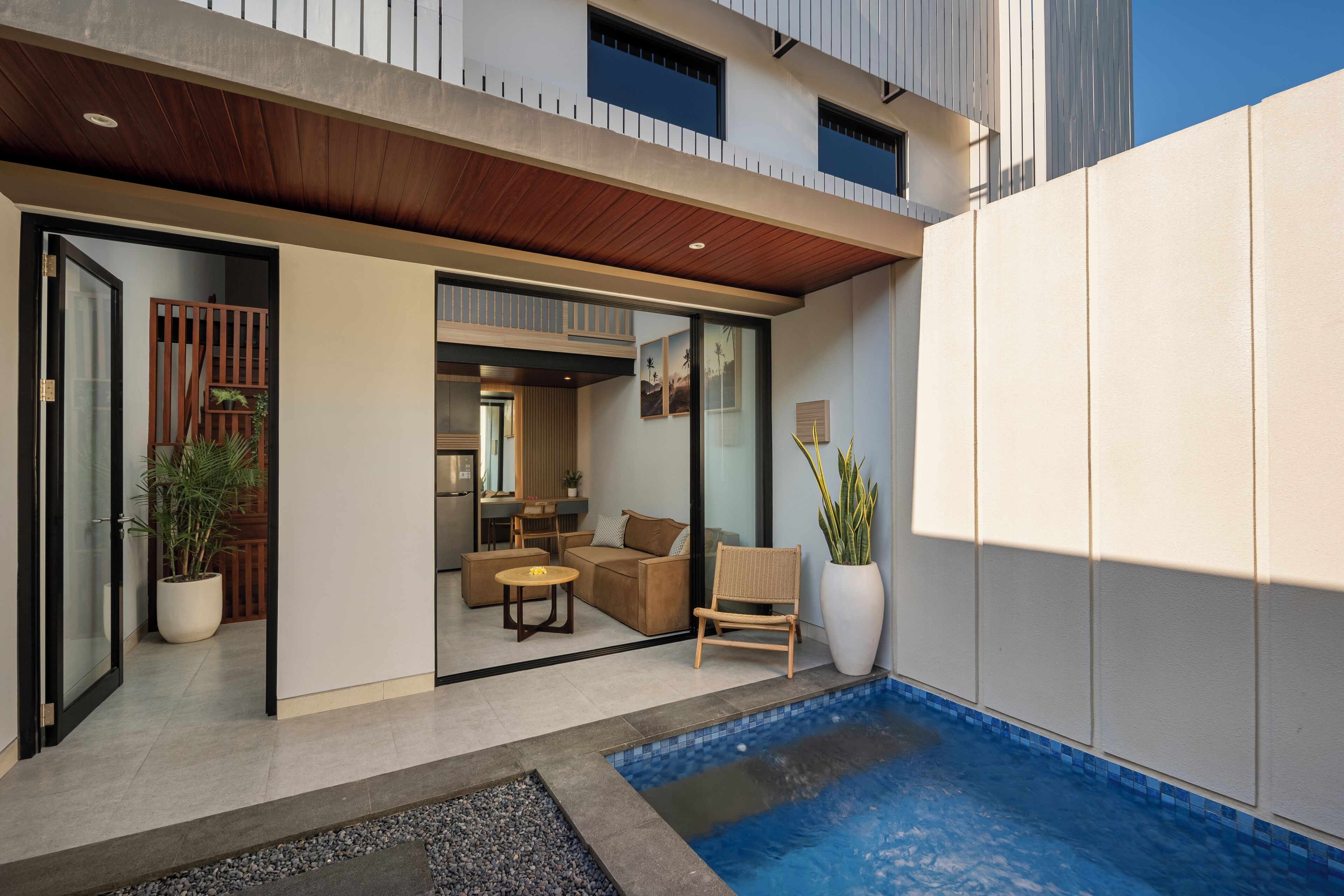 Un espacio exterior moderno con piscina, techo de madera y zona de estar con sofá y sillones.