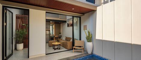 Un espacio exterior moderno con piscina, techo de madera y zona de estar con sofá y sillones.