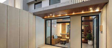 Une maison moderne avec une entrée dotée d’une porte en verre, une petite piscine et une terrasse en bois.