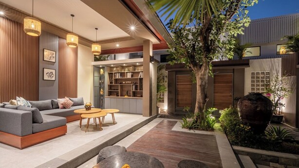 A modern living room with a sofa, coffee table, and pendant lights. There is a tree and a large vase in the outdoor area. - The New Moon Umalas (Kerobokan)