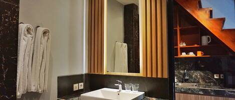 Un baño moderno con un espejo grande, un lavabo y una escalera de madera visible a través de la puerta de cristal.