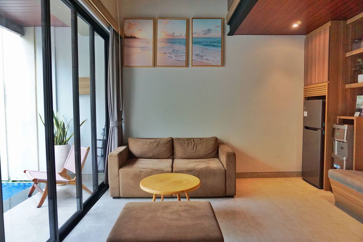 Una sala de estar moderna con un sofá color beige, una mesa de centro de madera y un ventanal que da a un balcón.