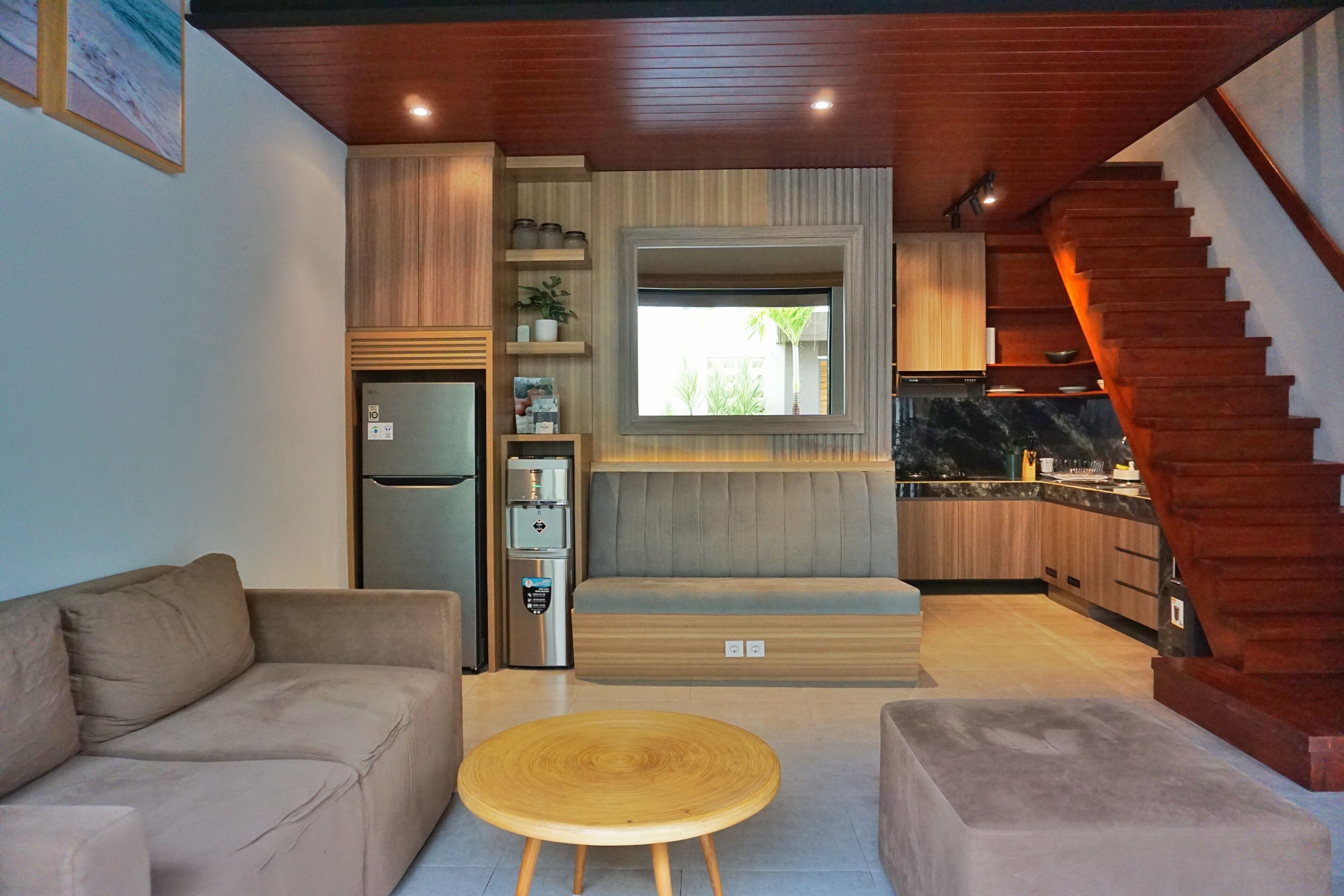 Una cocina moderna con estufa integrada, refrigerador y cafetera. Se ve una escalera de madera que sube a un nivel superior.