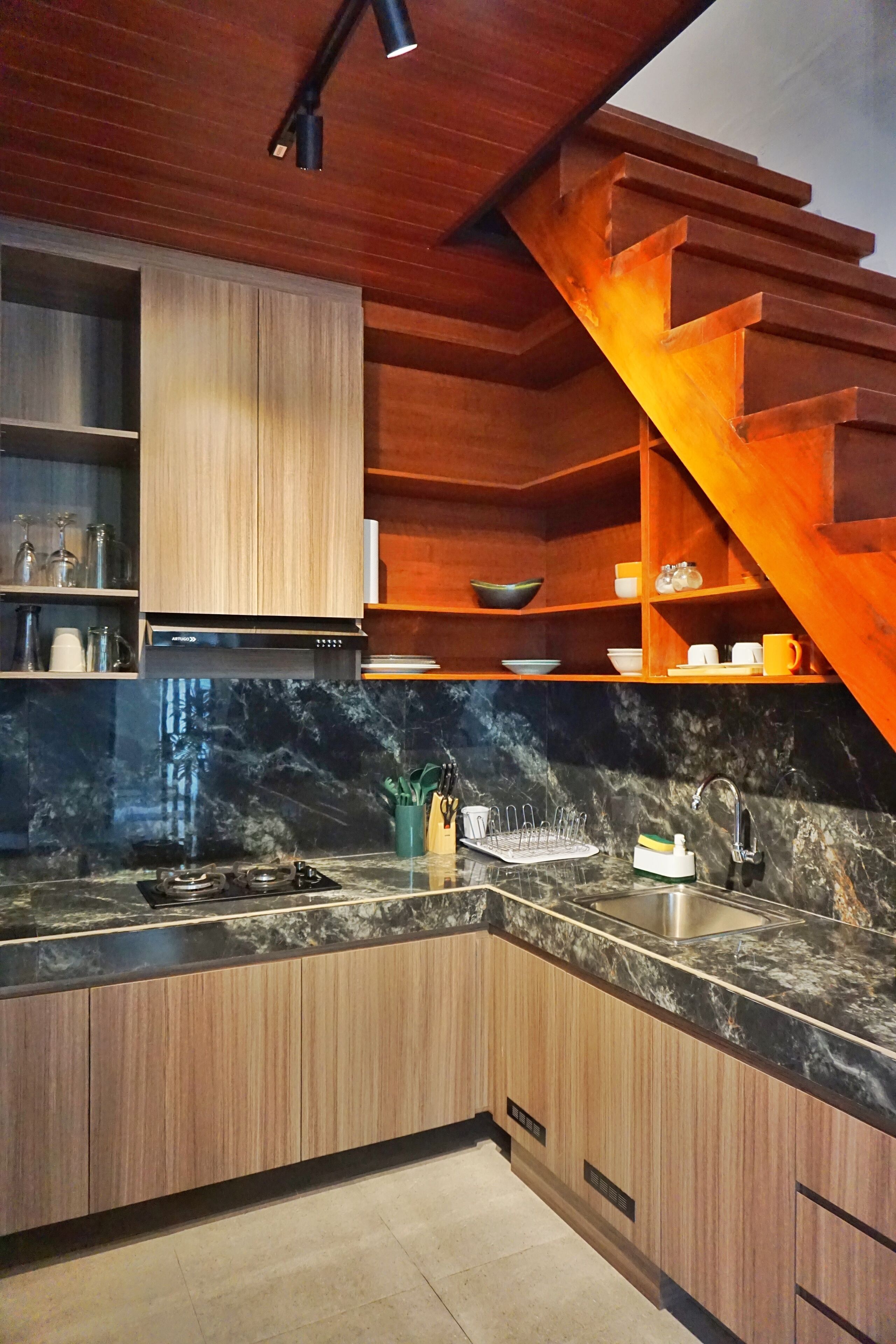 Eine Küche mit Holzschränken, einer Marmorarbeitsplatte, einem Gasherd und einem Edelstahlspülbecken.