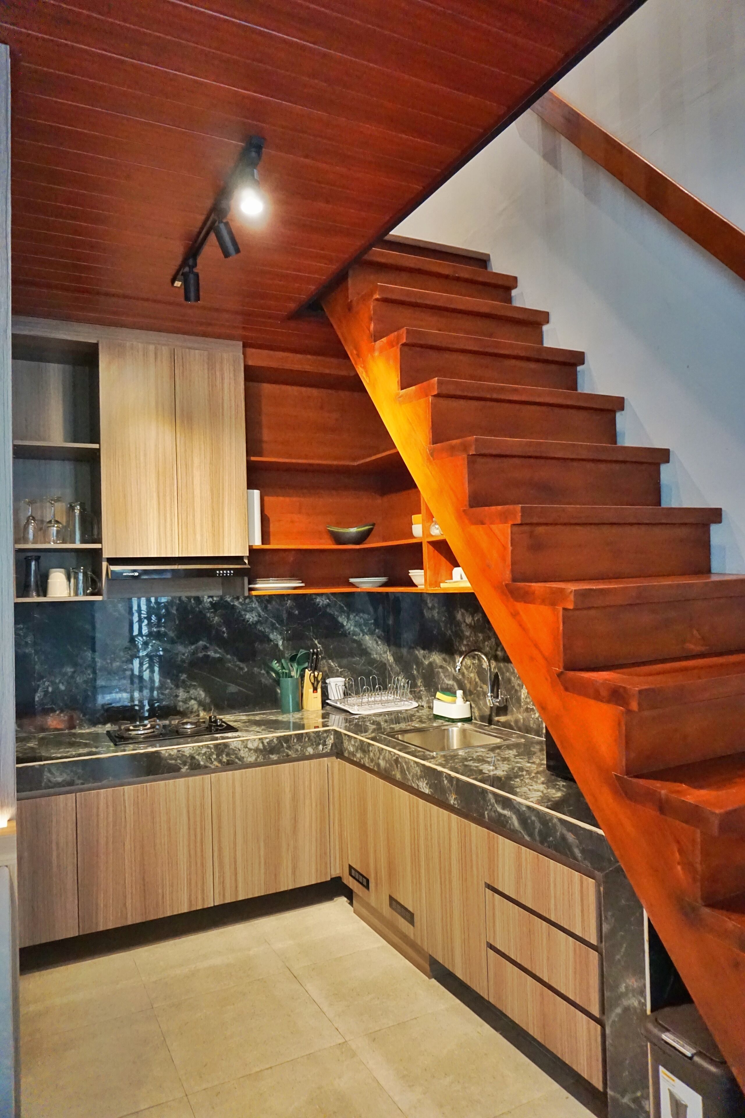 Une cuisine moderne avec des meubles en bois, un plan de travail en marbre et un escalier en bois doté d’un éclairage intégré.