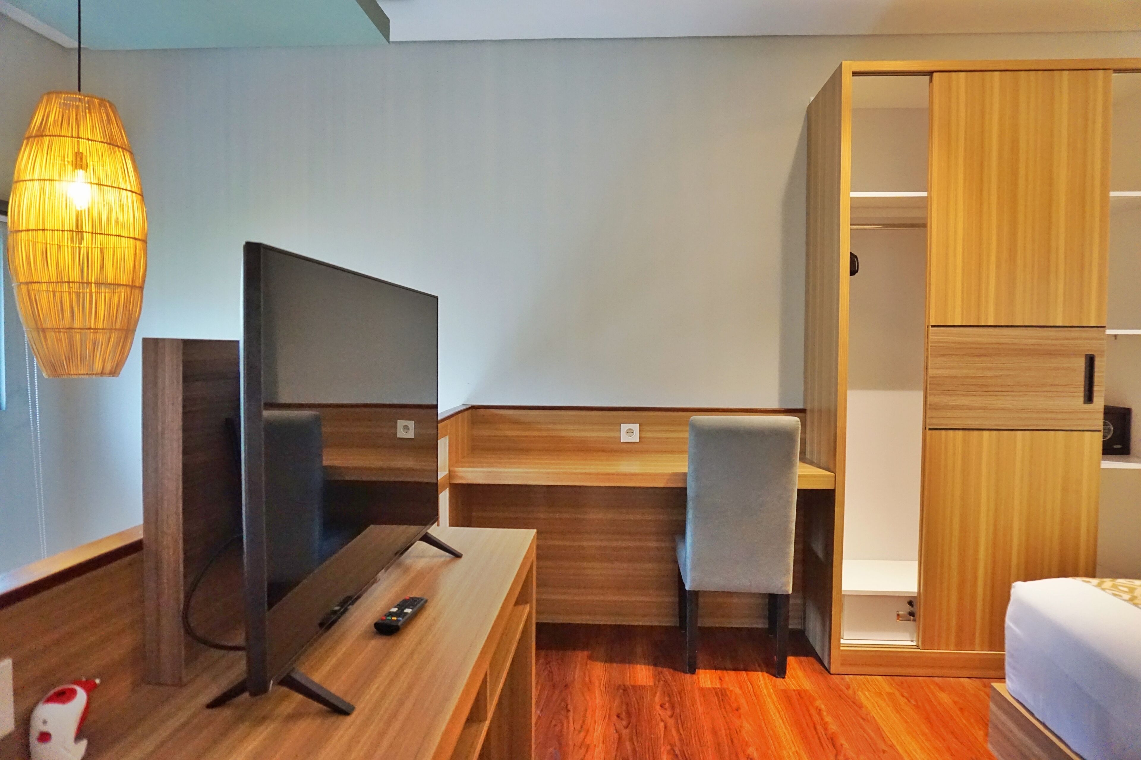 Una habitación de hotel moderna con un escritorio de madera, televisión, una silla y un armario.