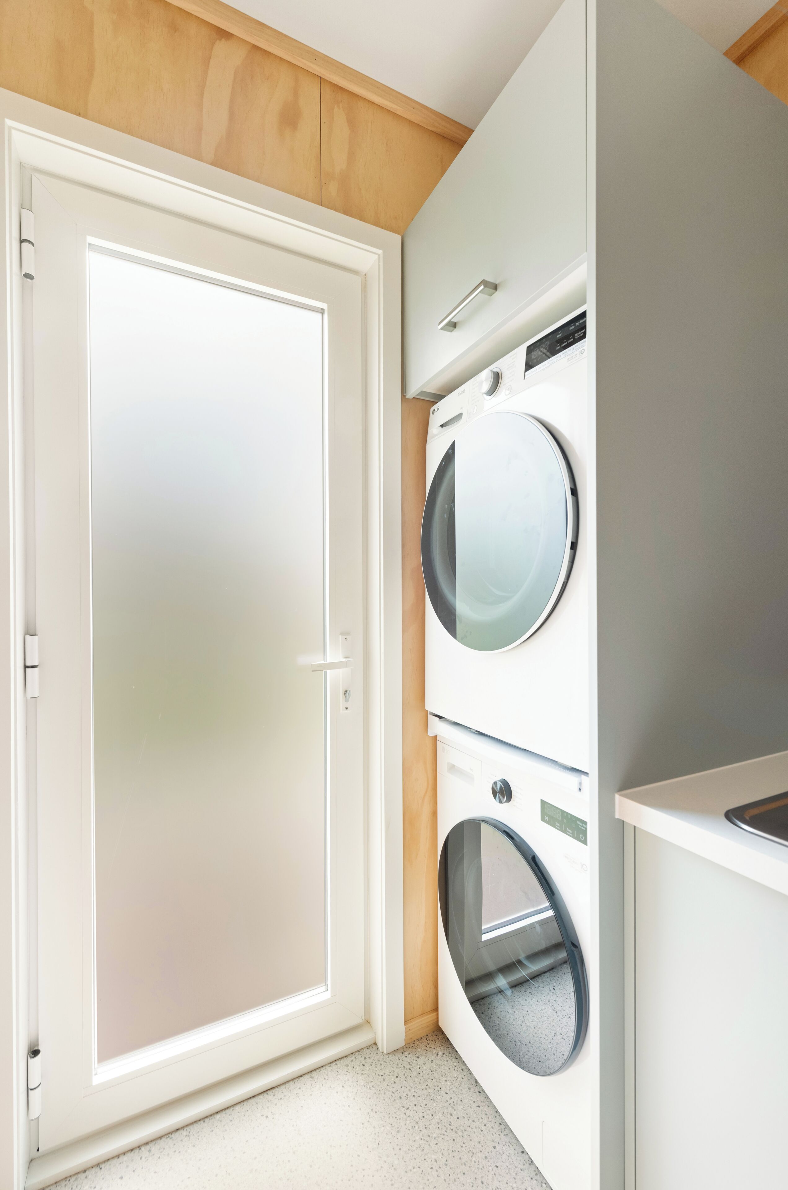 A laundry room with a closed door, two stacked washing machines, and a wooden ceiling.