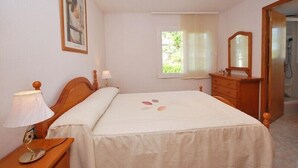 Een slaapkamer met een bed, nachtkastje, lamp, dressoir, spiegel en een raam met gordijnen.