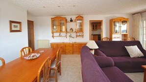 Een woonkamer met een houten eettafel, een paarse bank en houten kasten met glazen deuren.