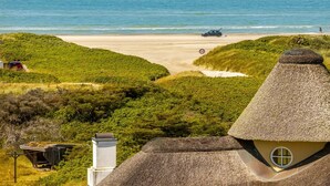 Blick auf einen Strand mit einem Haus mit Reetdach, einem Geschwindigkeitsbegrenzungsschild und einem geparkten Auto.