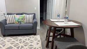 Una sala de estar con un sofá gris, un tapete estampado y una mesa de madera con dos botellas de agua.