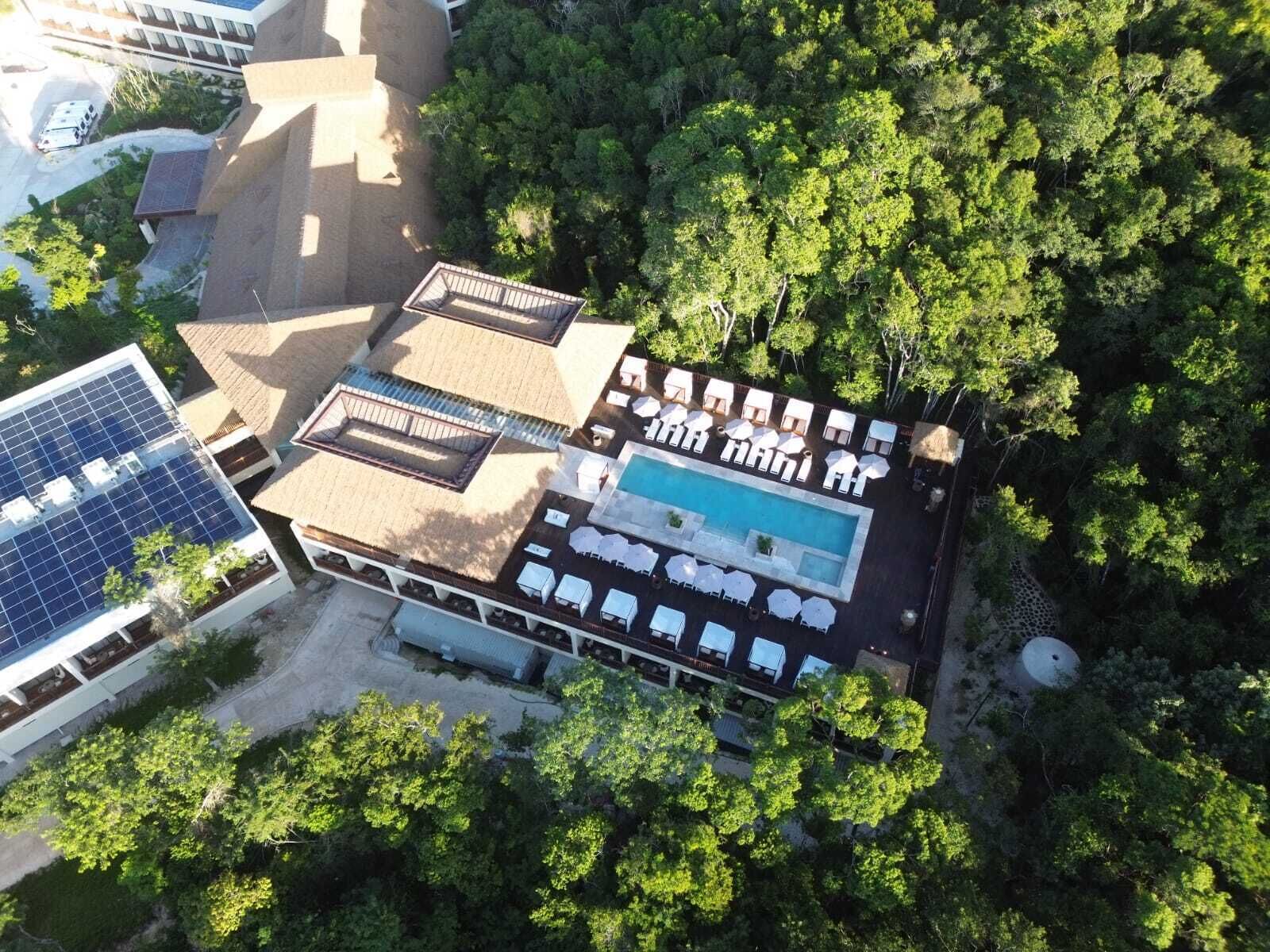 An aerial view of a resort with a swimming pool, sun loungers, and solar panels.