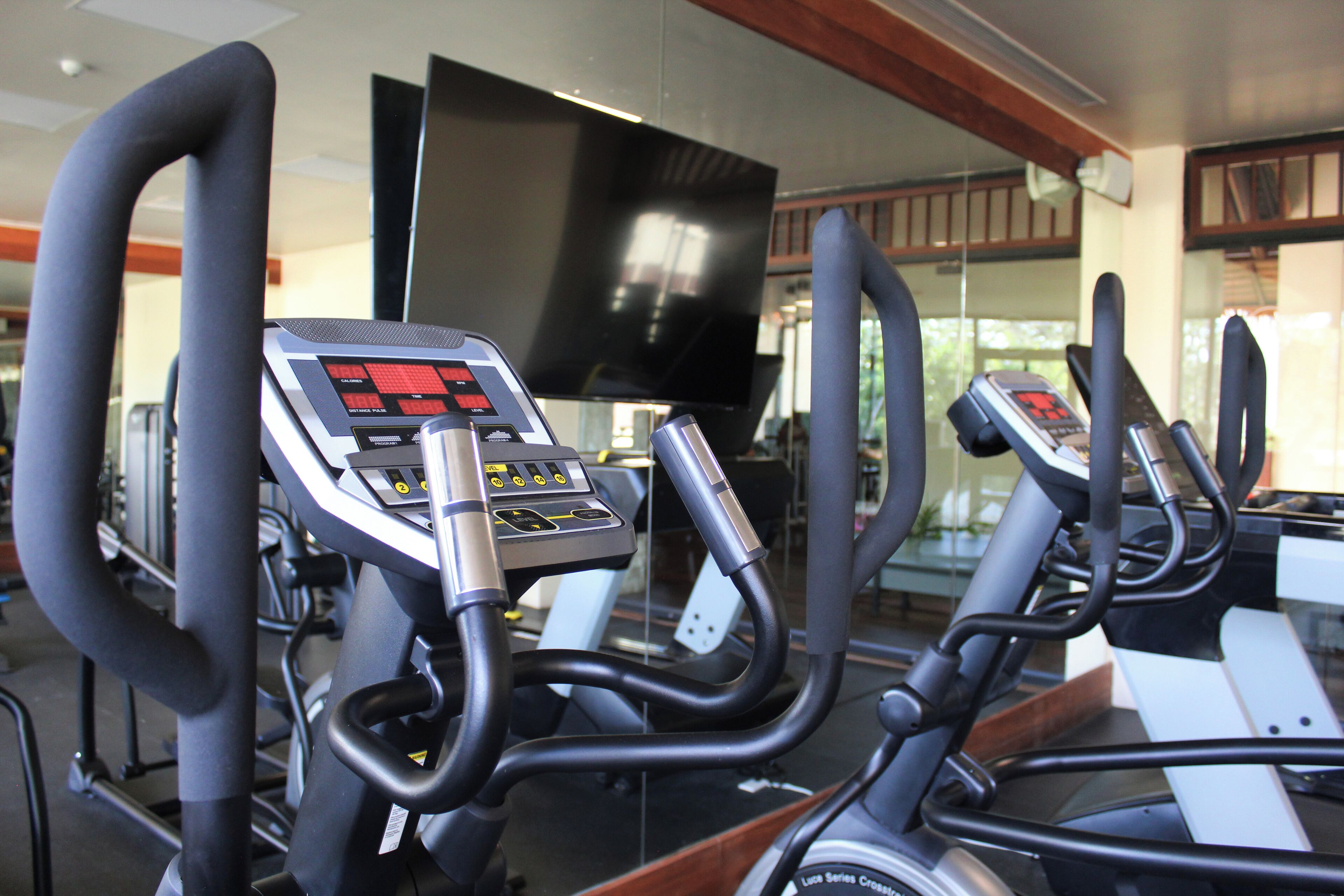 A row of stationary bikes in a gym with a large TV mounted on the wall.