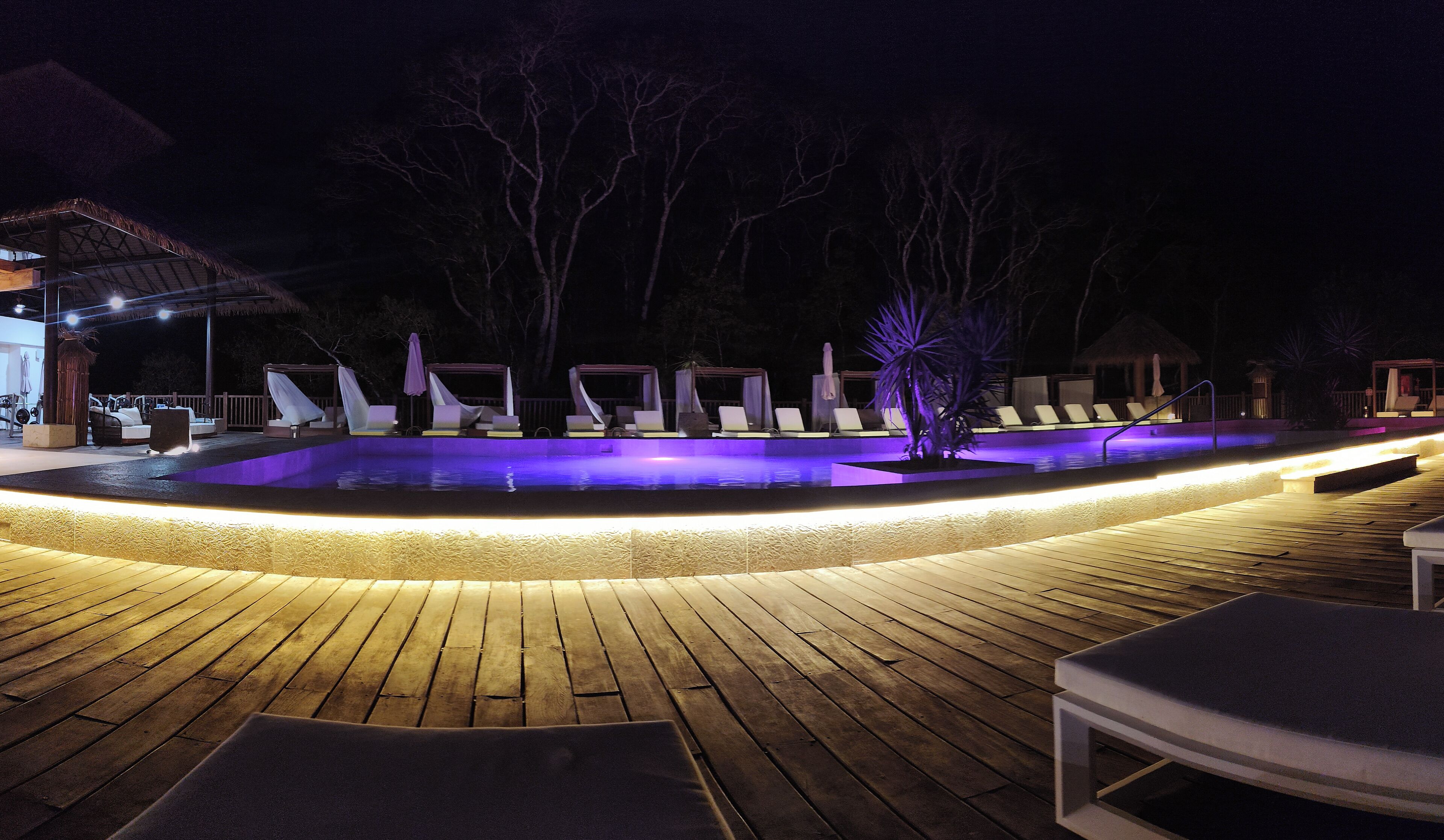 Un área de piscina nocturna con sillones de descanso y una terraza de madera.