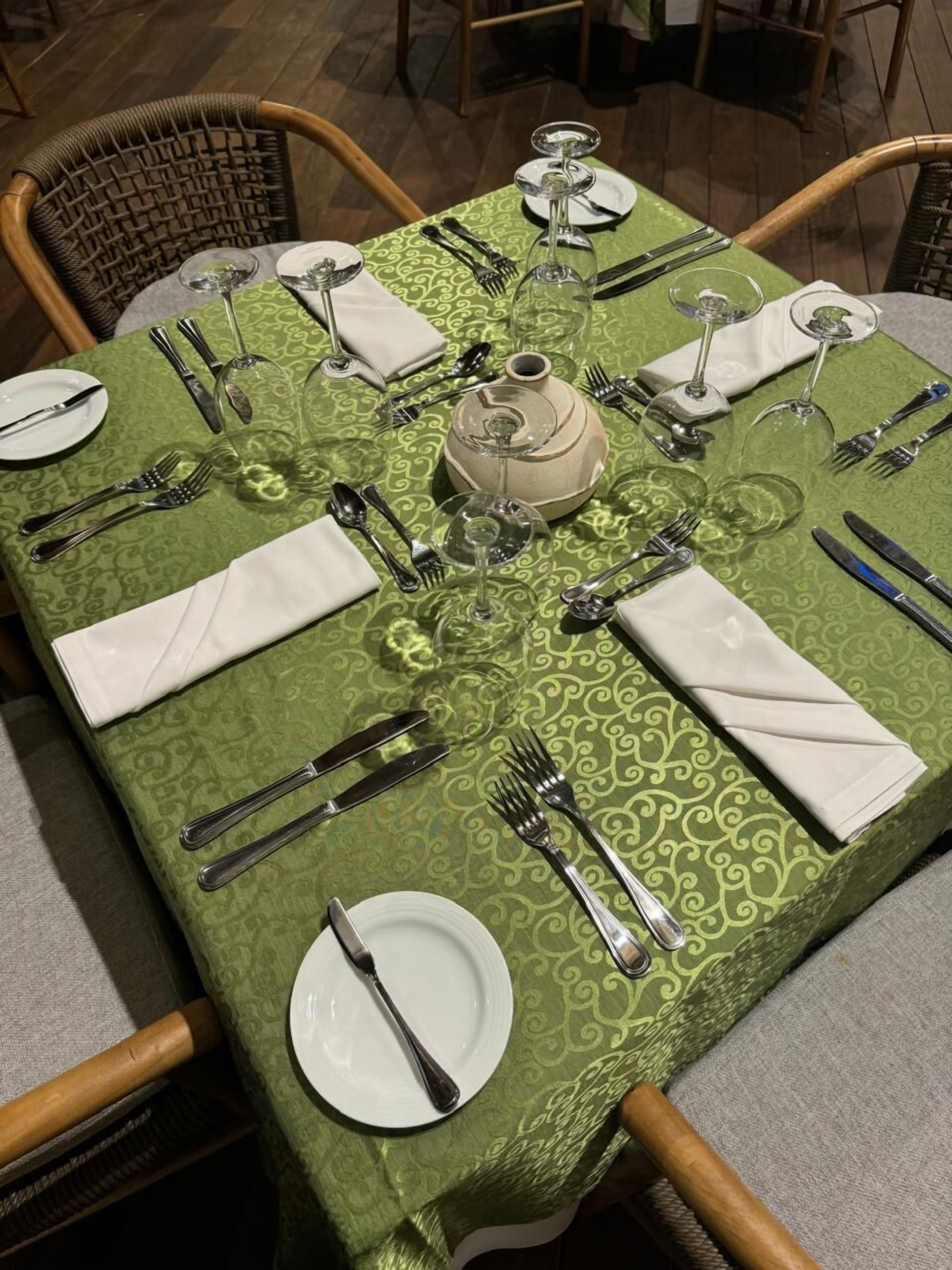 A dining table set with white plates, silverware, and clear wine glasses, centered around a decorative ceramic pot.