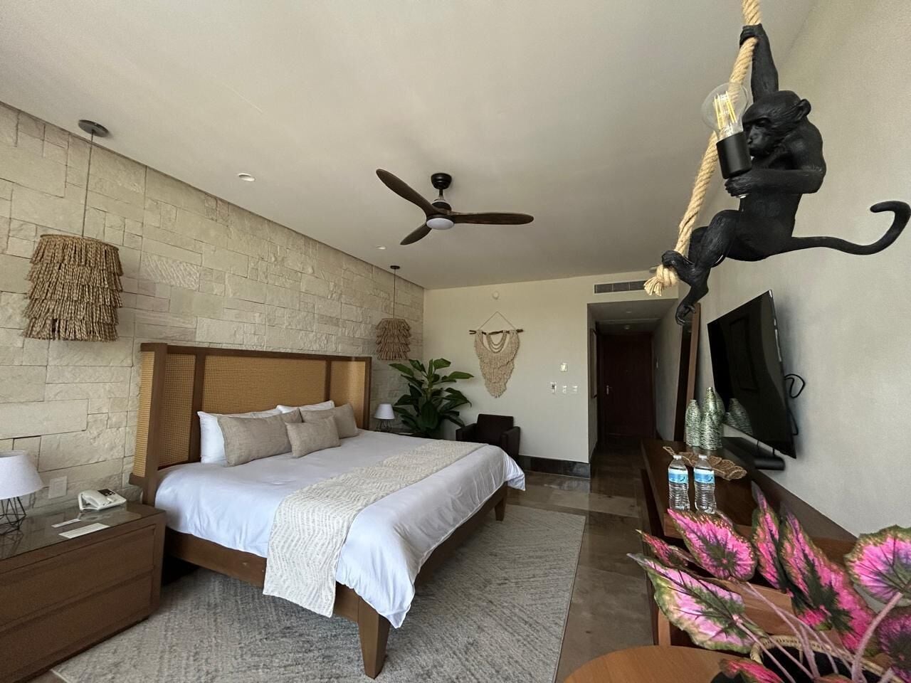 Ein Schlafzimmer mit einem Bett, Nachttischen, einem Deckenventilator, einem Fernseher und einer dekorativen Affine Skulptur.