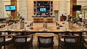 Un restaurante espacioso con una larga mesa de comedor, sillas de mimbre, una zona de bar y una pantalla de televisión.