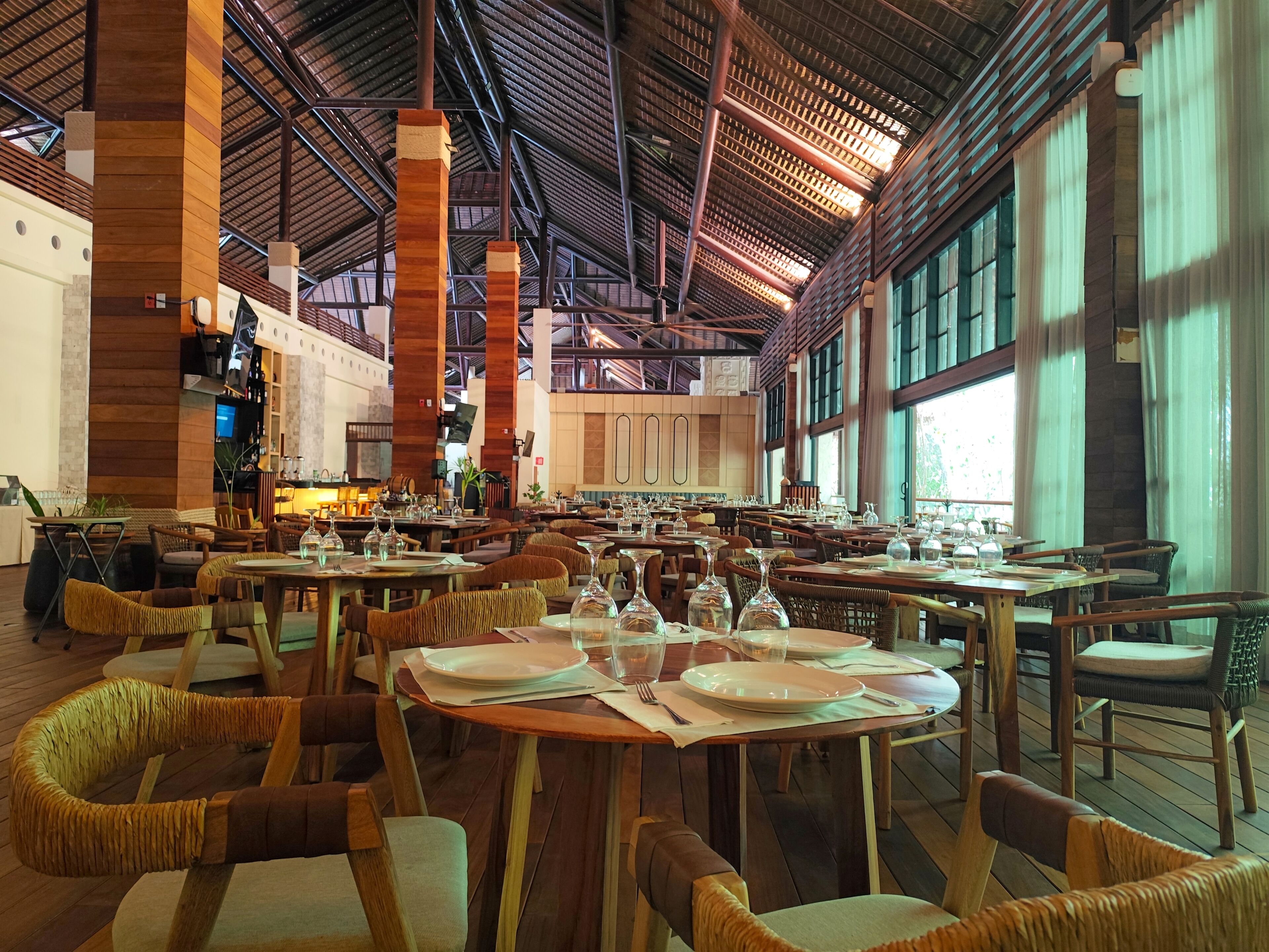 A spacious restaurant with high ceilings, large windows, and wooden furniture.