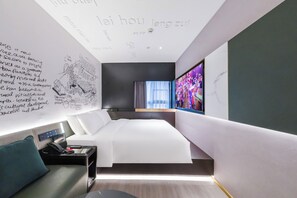 A modern hotel room with a large bed, a desk, and a TV.