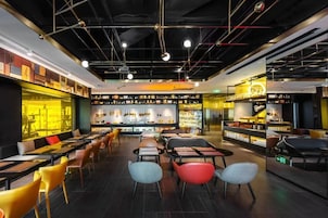 Un interno ristorante moderno con soffitti alti, condotti a vista e diverse tipologie di posti a sedere, tra cui tavoli e sedie.